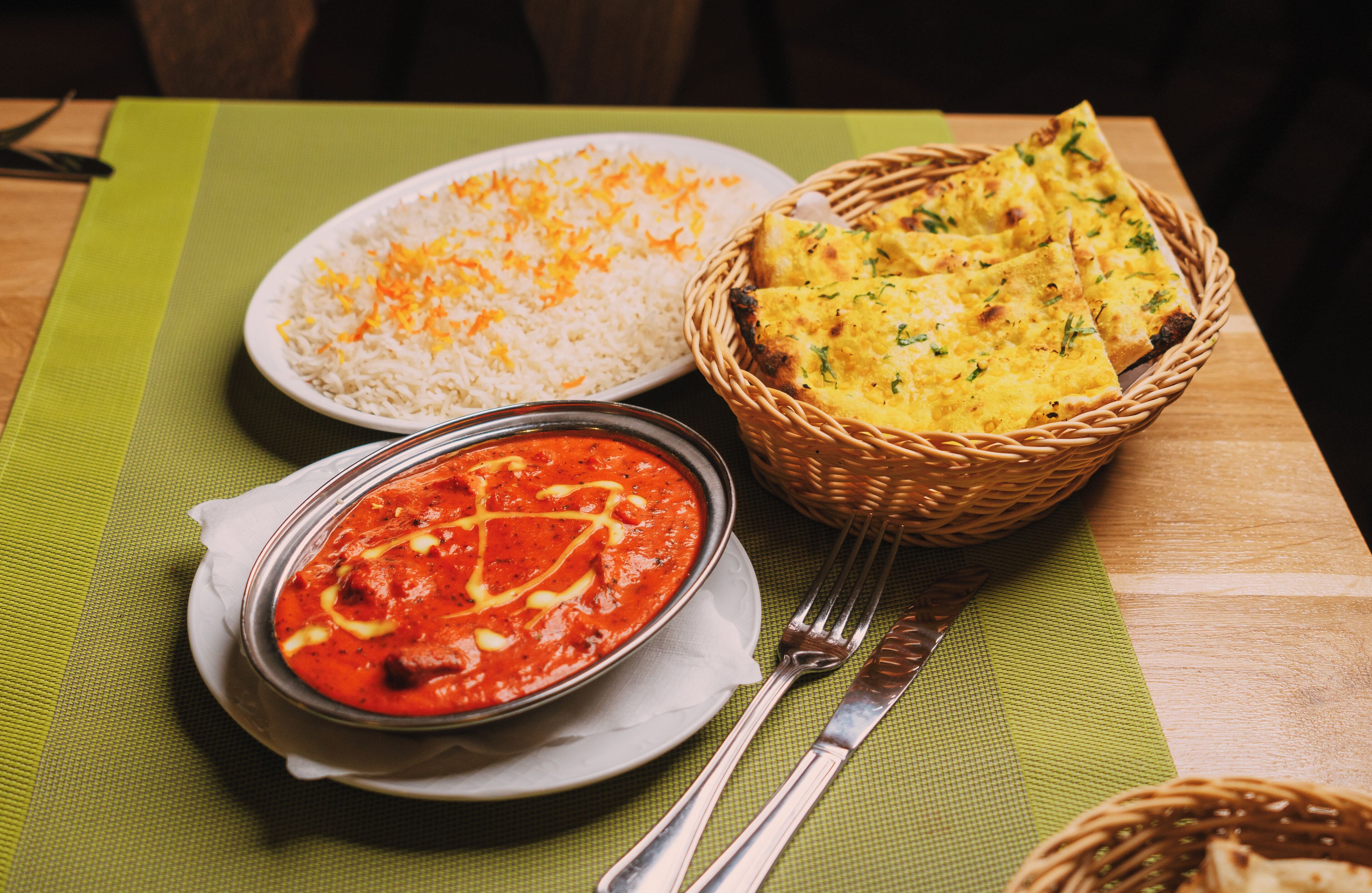 Ein Tisch mit einer Schüssel weißem Reis, einem Korb mit Naan-Brot und einer Schale rote Curry.