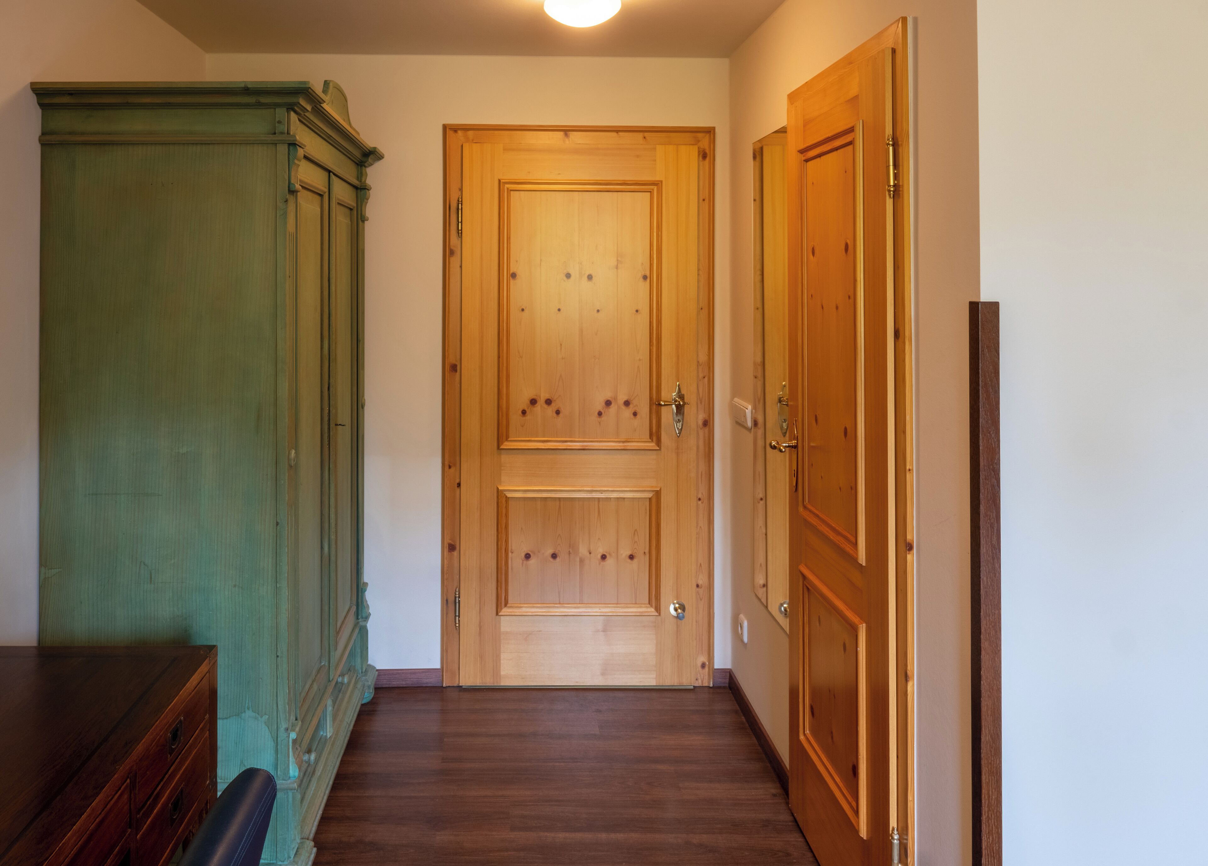 Een hal met een houten deur, een groen kastje en een houten dressoir.