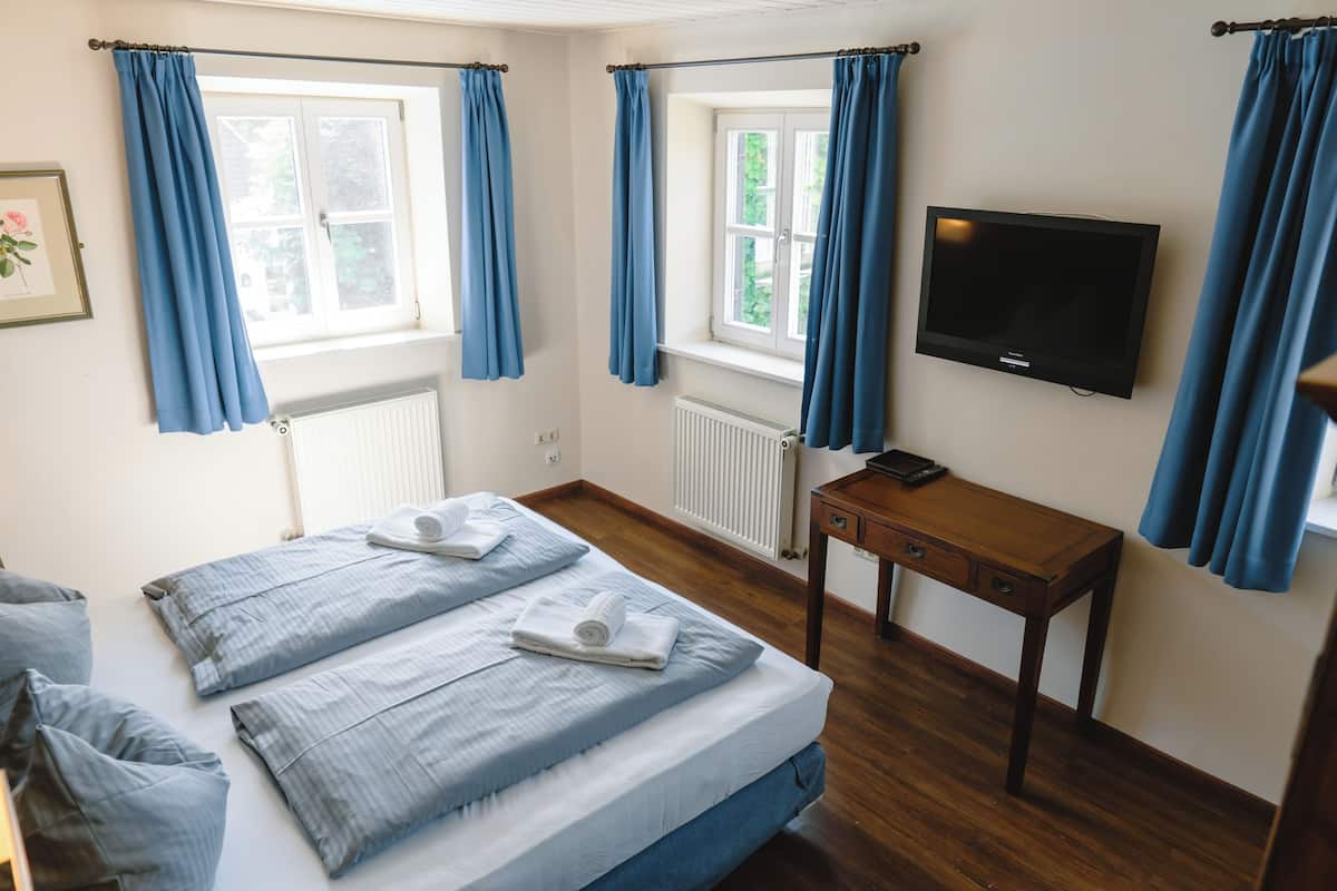 A hotel room with two beds, a wooden desk, a television, and blue curtains.