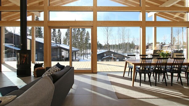 A spacious living room with a large glass door leading to a deck, a fireplace, and a dining area with chairs and a table. - Eerikkilä Sport & Outdoor Resort (Tammela)
