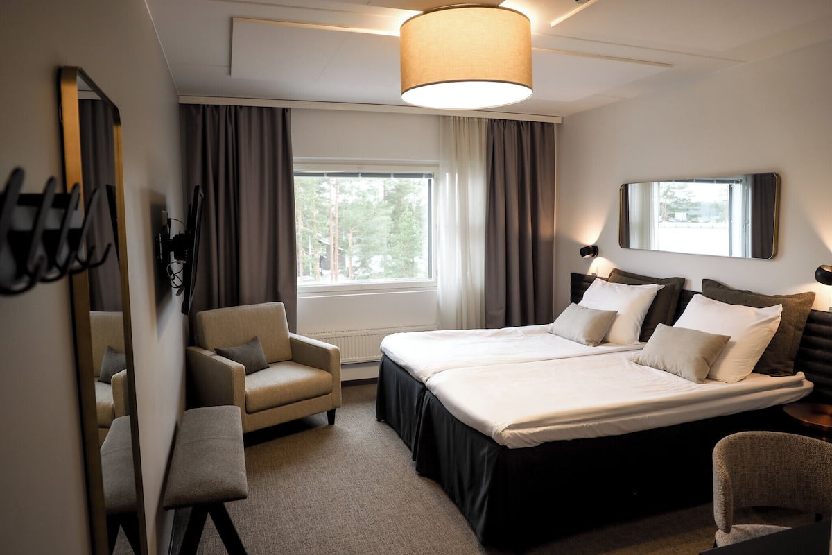 A hotel room with a large bed, a chair, a desk, a mirror, and a window with curtains.