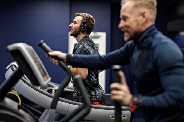 Une salle de sport avec des tapis de course, et une personne qui en utilise un.
