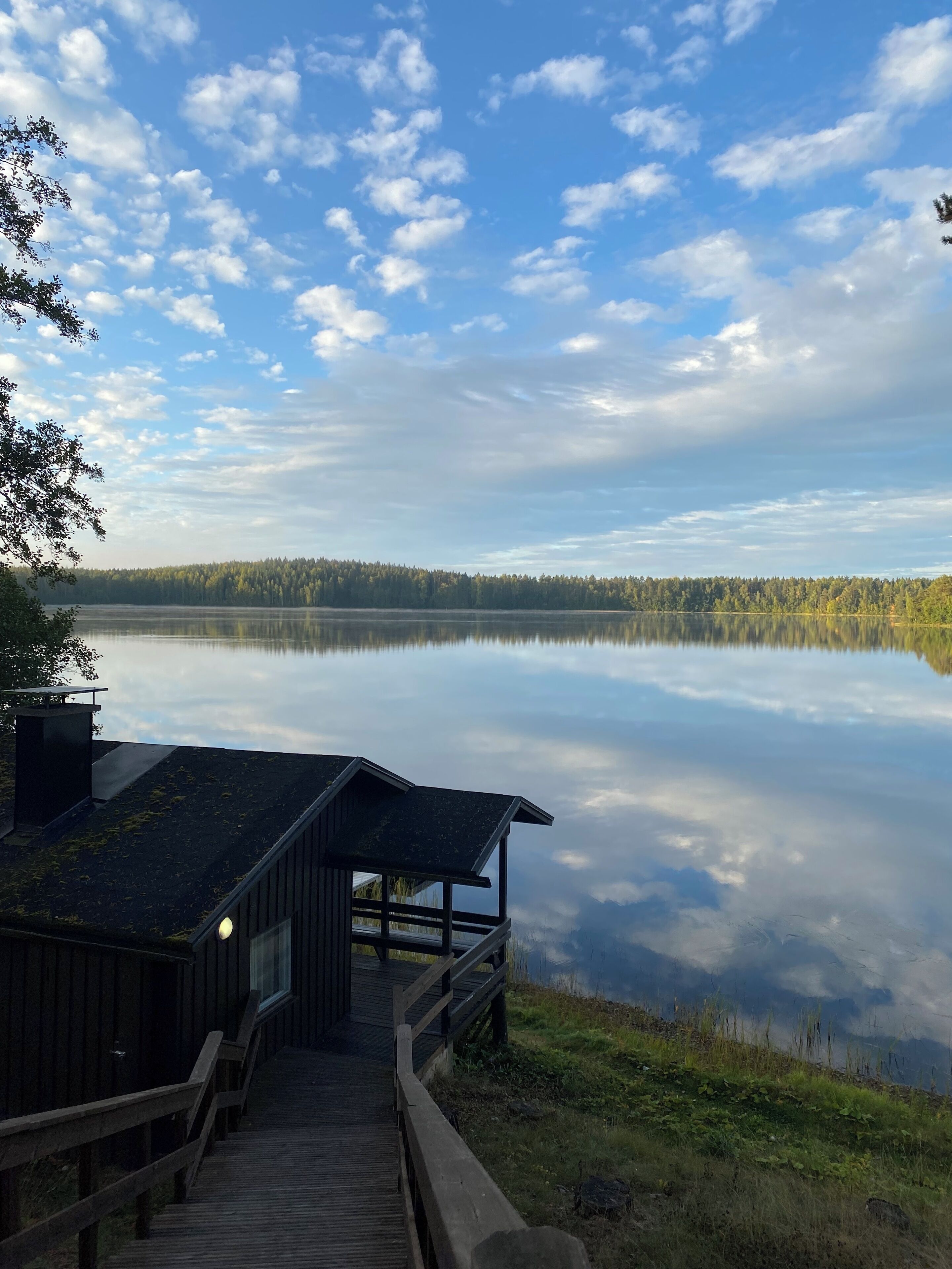 A wooden dock leading to a cabin with a glass door, overlooking a calm lake with a forested shoreline.
