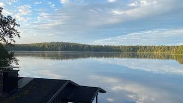A wooden dock leading to a cabin with a glass door, overlooking a calm lake with a forested shoreline.