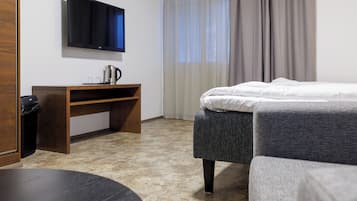A hotel room with a bed, a desk with a television, a coffee maker, and a trash bin.