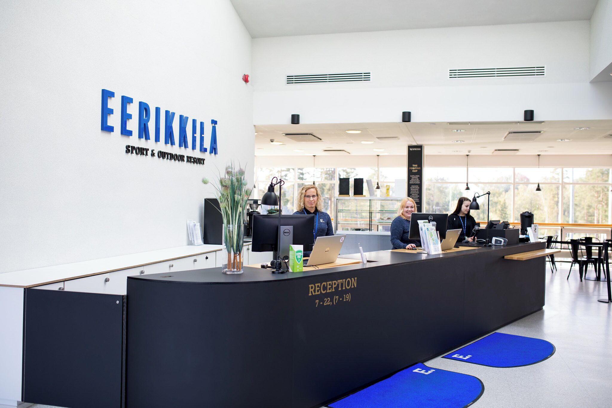 Mostrador de recepción en el EERIKKILA Sport & Outdoor Resort, con tres empleados, una señalización y una zona de recepción.