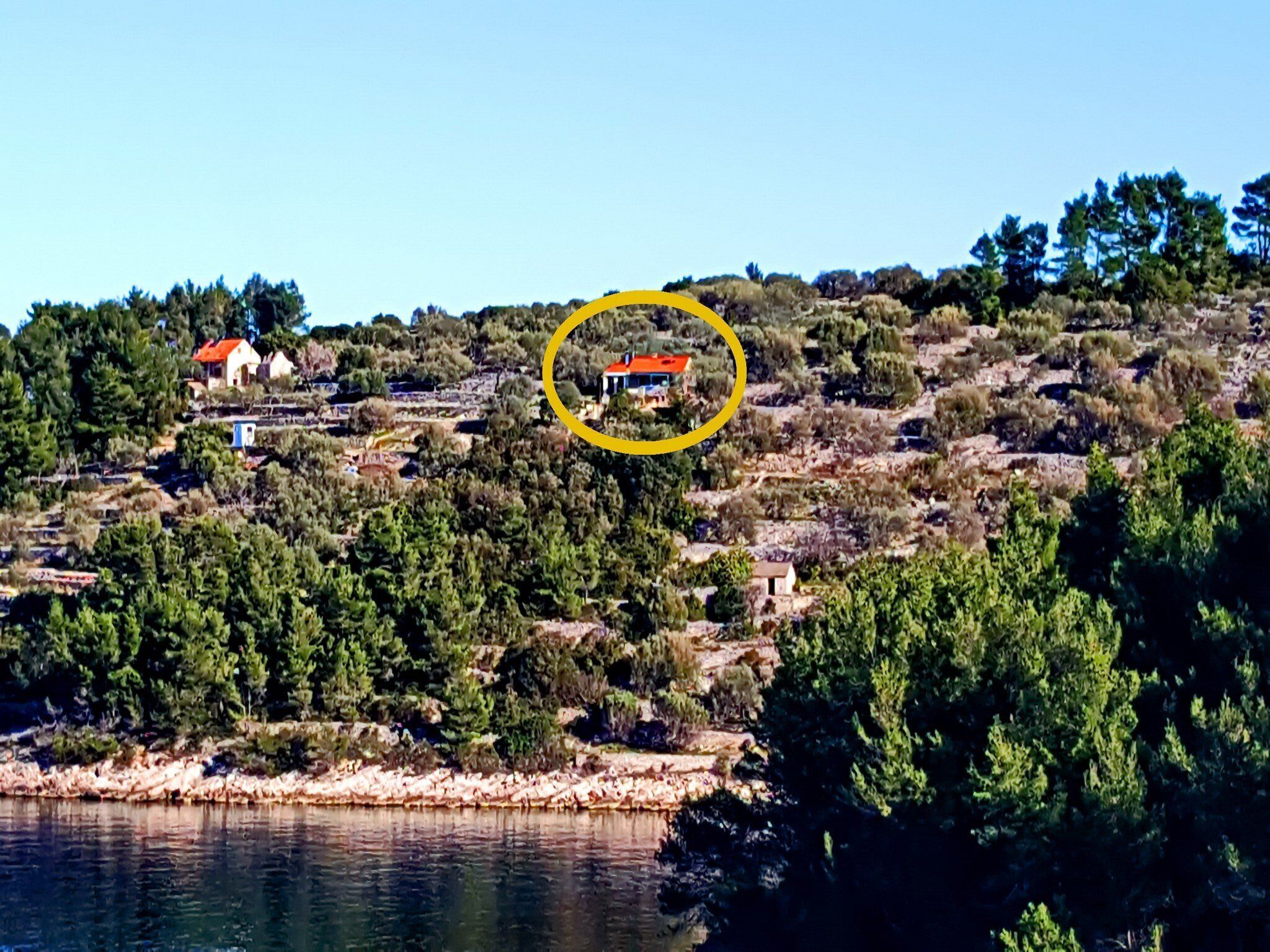 Un paysage côtier avec un petit bâtiment mis en évidence, entouré d’une végétation luxuriante et bordé par une étendue d’eau.
