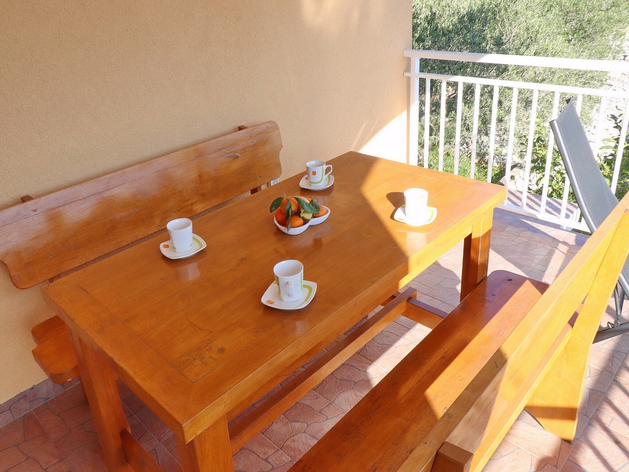 A wooden table with four white cups and saucers, a bowl of fruit, and a bench.