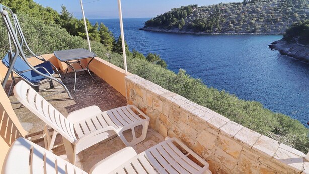 A terrace with white plastic chairs and a table overlooking a coastal area with a stone wall and a view of the sea. - Peaceful Holiday House Senija (Vela Luka)