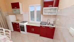 A compact kitchen with red cabinets, a white stove, and a window. - Peaceful Holiday House Senija (Vela Luka)