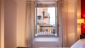 Hotellihuone, jossa on sänky, ikkuna verhoilla ja näkymä ulkona olevaan rakennukseen.