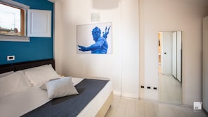 A bedroom with a bed, a window, a wall-mounted artwork, and a mirror.