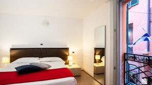 A hotel room with a bed, bedside lamps, a window with a view of the street, and a door to the balcony.