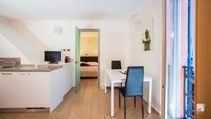 A compact hotel room with a kitchenette, a bed, a dining area, and a view of the outside.