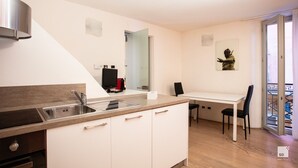 A modern kitchen with a built-in stove, sink, and white cabinetry. There is a dining area with a table and chairs, and a small statue on the wall.