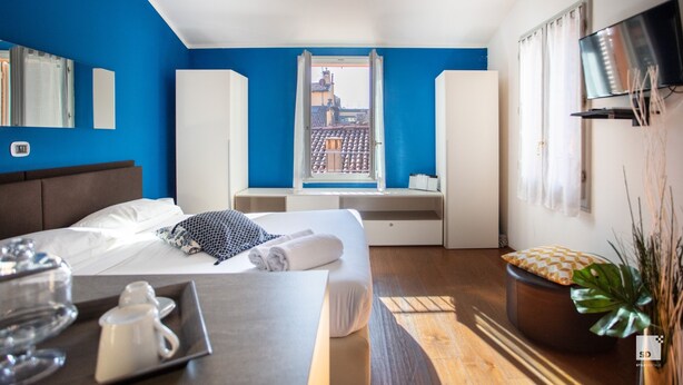 A hotel room with a bed, a TV, a window with a city view, and a bedside table with a tray of items.