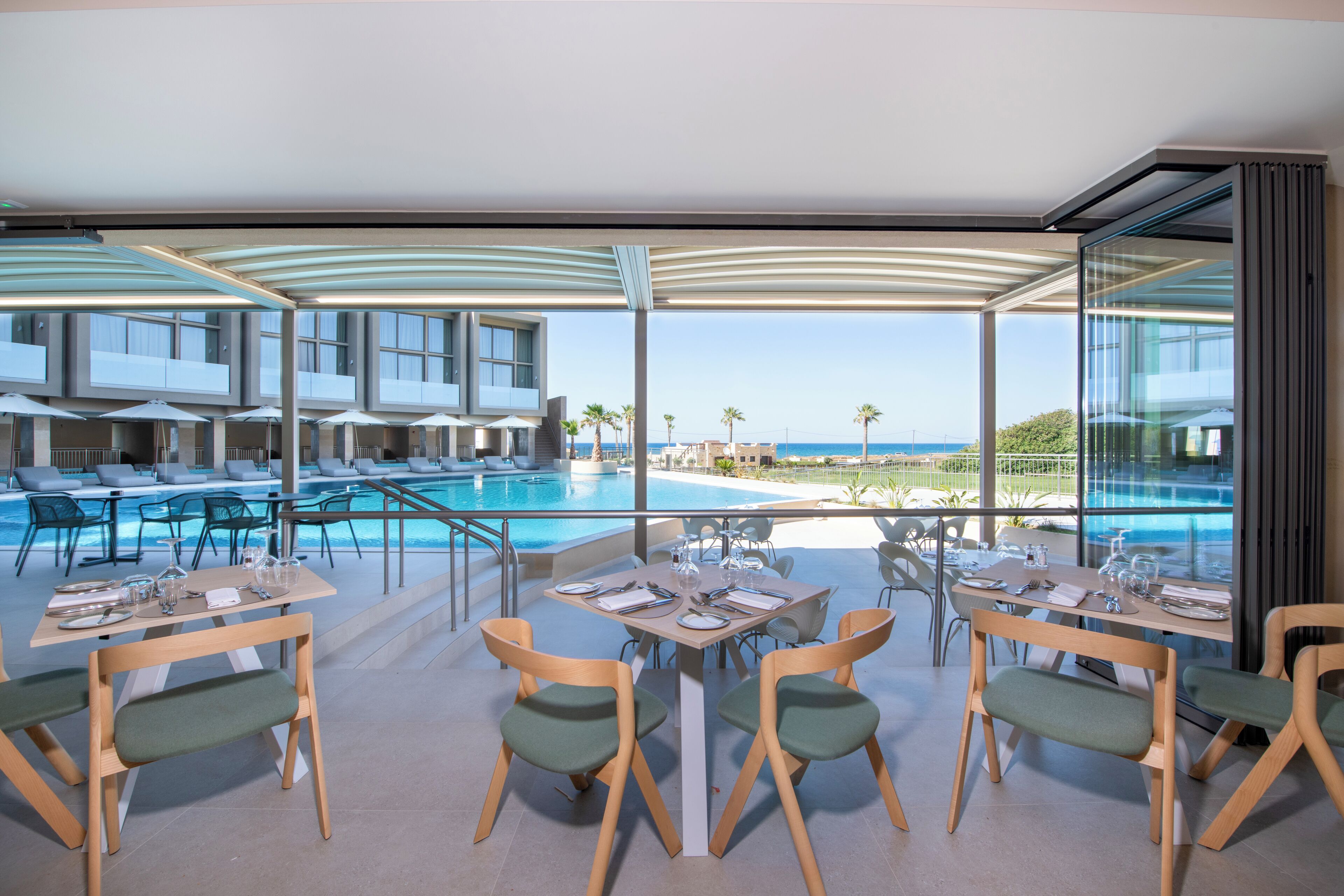 A modern outdoor dining area with a pool view, multiple tables, and chairs.