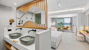 Habitación de hotel moderna con una cama grande, dos lavamanos, un espejo con marco de madera y un balcón con vistas al mar.