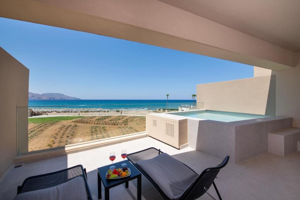 A balcony with a view of the beach, a hot tub, and a table with fruit and wine glasses.
