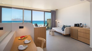 Una habitación de hotel moderna con un ventanal que ofrece vista al océano, una mesa de madera con una bandeja de frutas, un sofá y una pequeña mesa de centro.