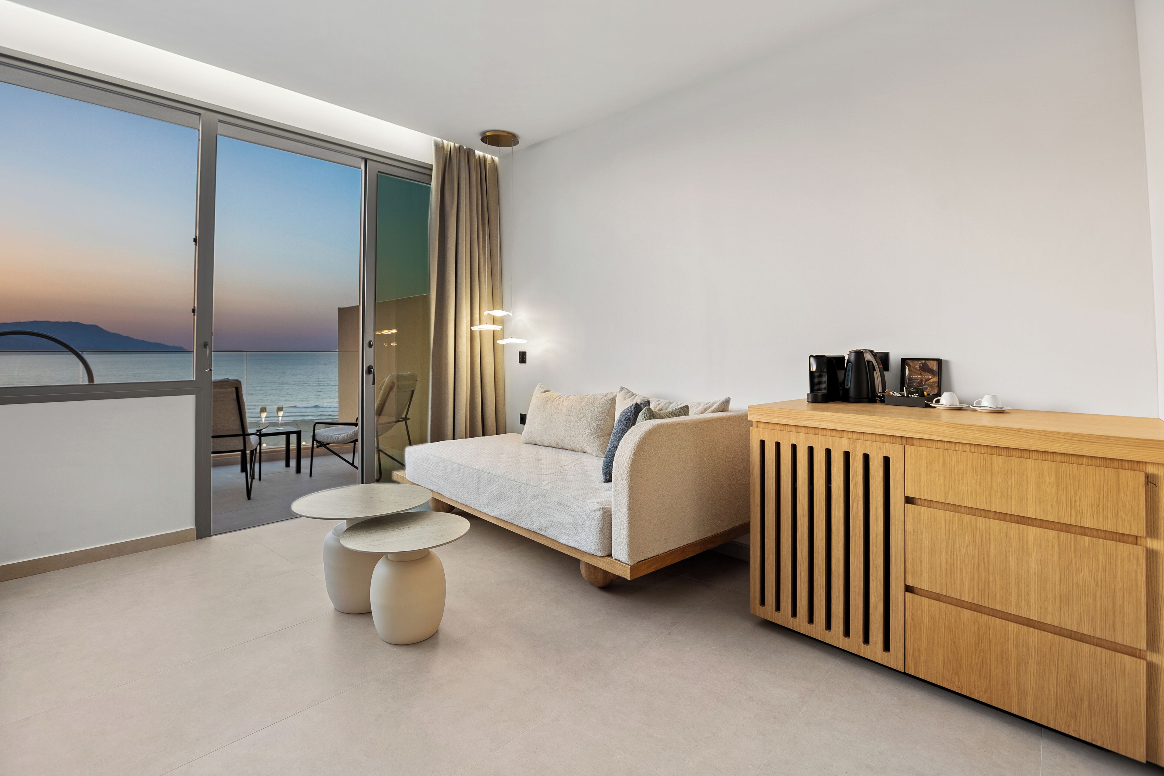 Habitación de hotel moderna con sofá, aparador de madera y balcón con vista al mar.