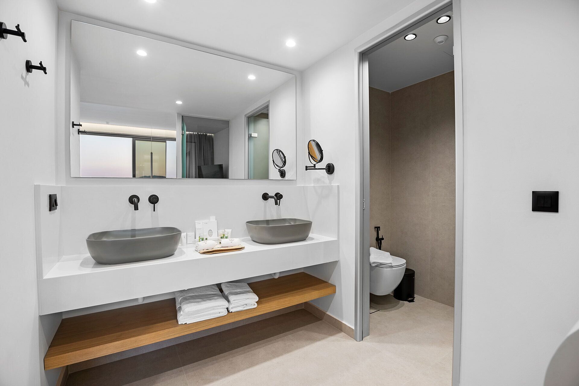 A modern bathroom with two vessel sinks, a large mirror, and a toilet.