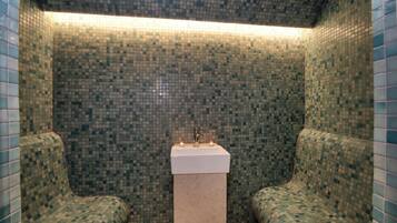 Bathroom features a pedestal sink, lit candle, and two benches for seating.