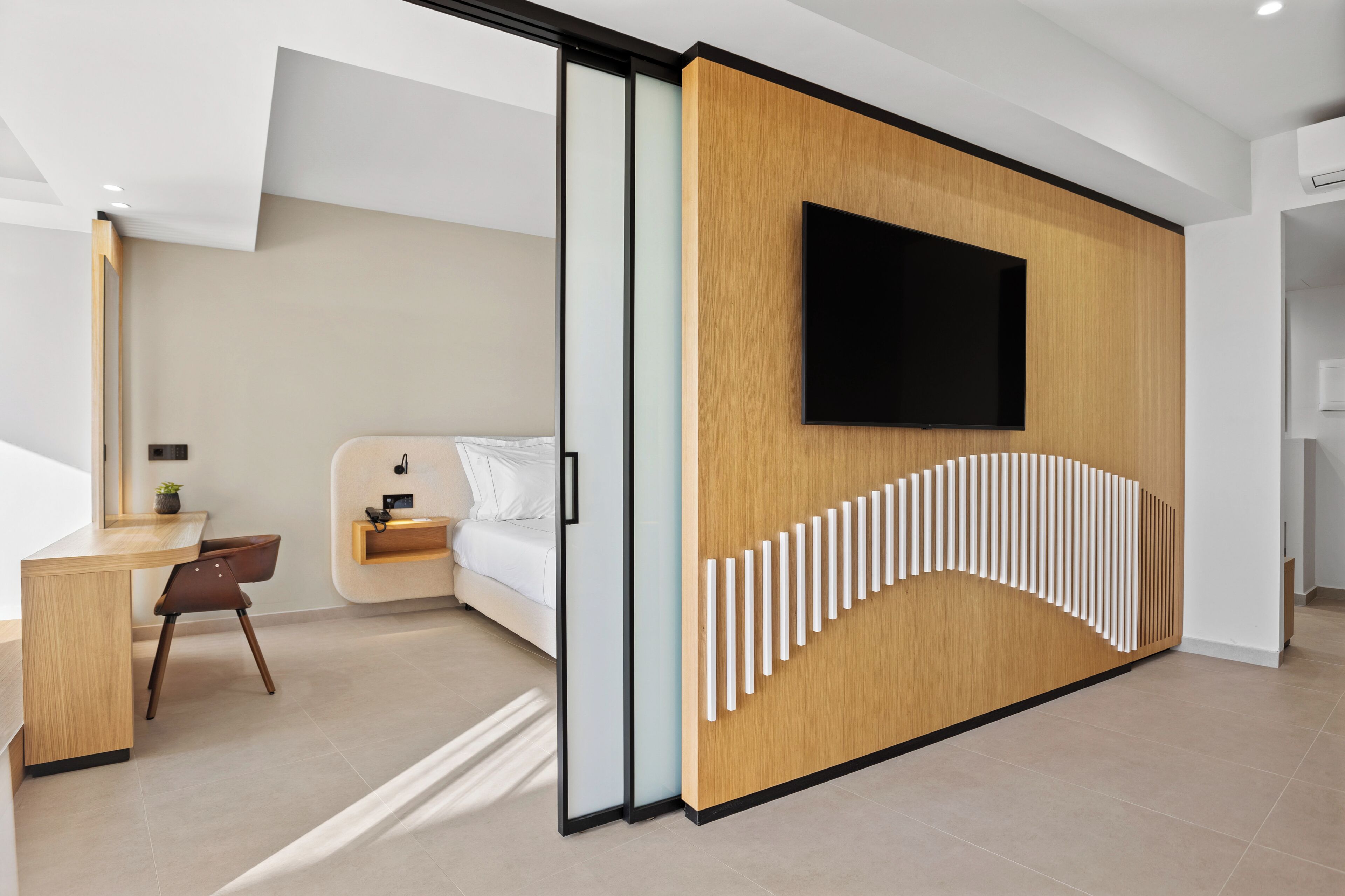 Ein modernes Hotelzimmer mit einer Wand in Holzoptik, einem Flachbildfernseher, einem Bett, einem Schreibtisch und einem Stuhl.
