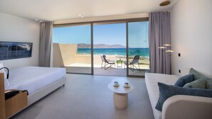 Una habitación de hotel moderna con una cama grande, un sofá, una mesita con tazas y un balcón con vista al mar.