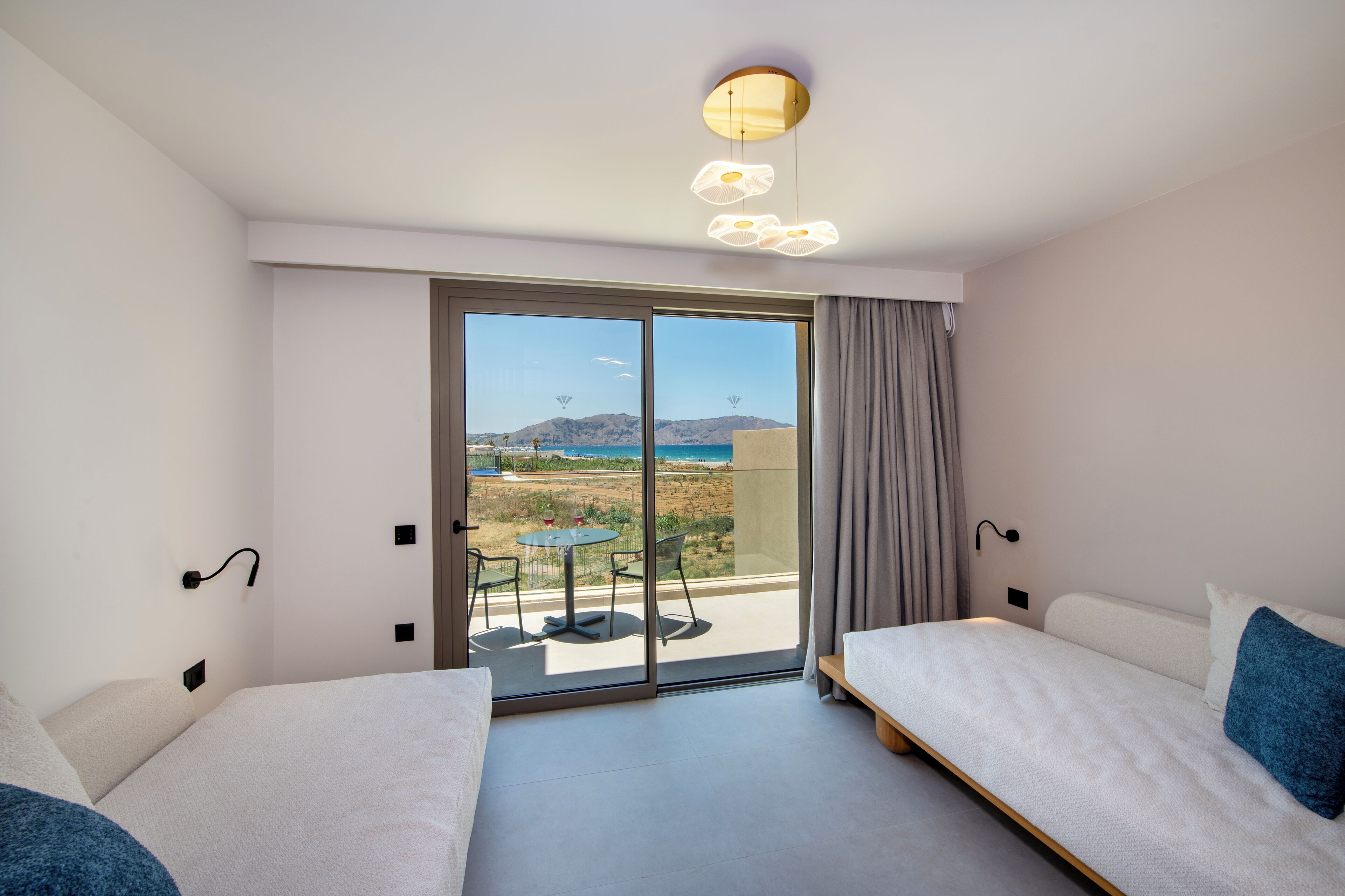 A hotel room with a balcony, a bed, a table, and a view of the beach.