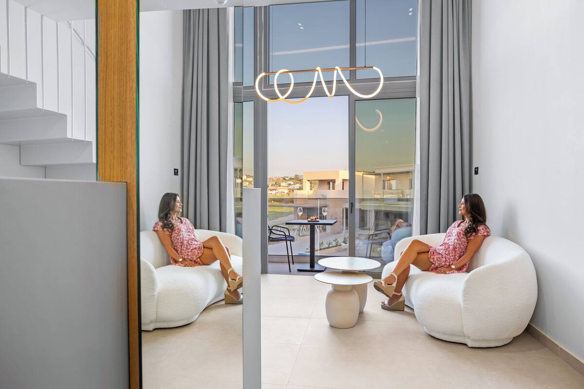 A modern interior with two white, round seating areas and a glass wall offering a view of the outdoors.