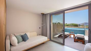 A modern bedroom with a sofa, a glass door leading to a balcony with a pool and lounge chairs.