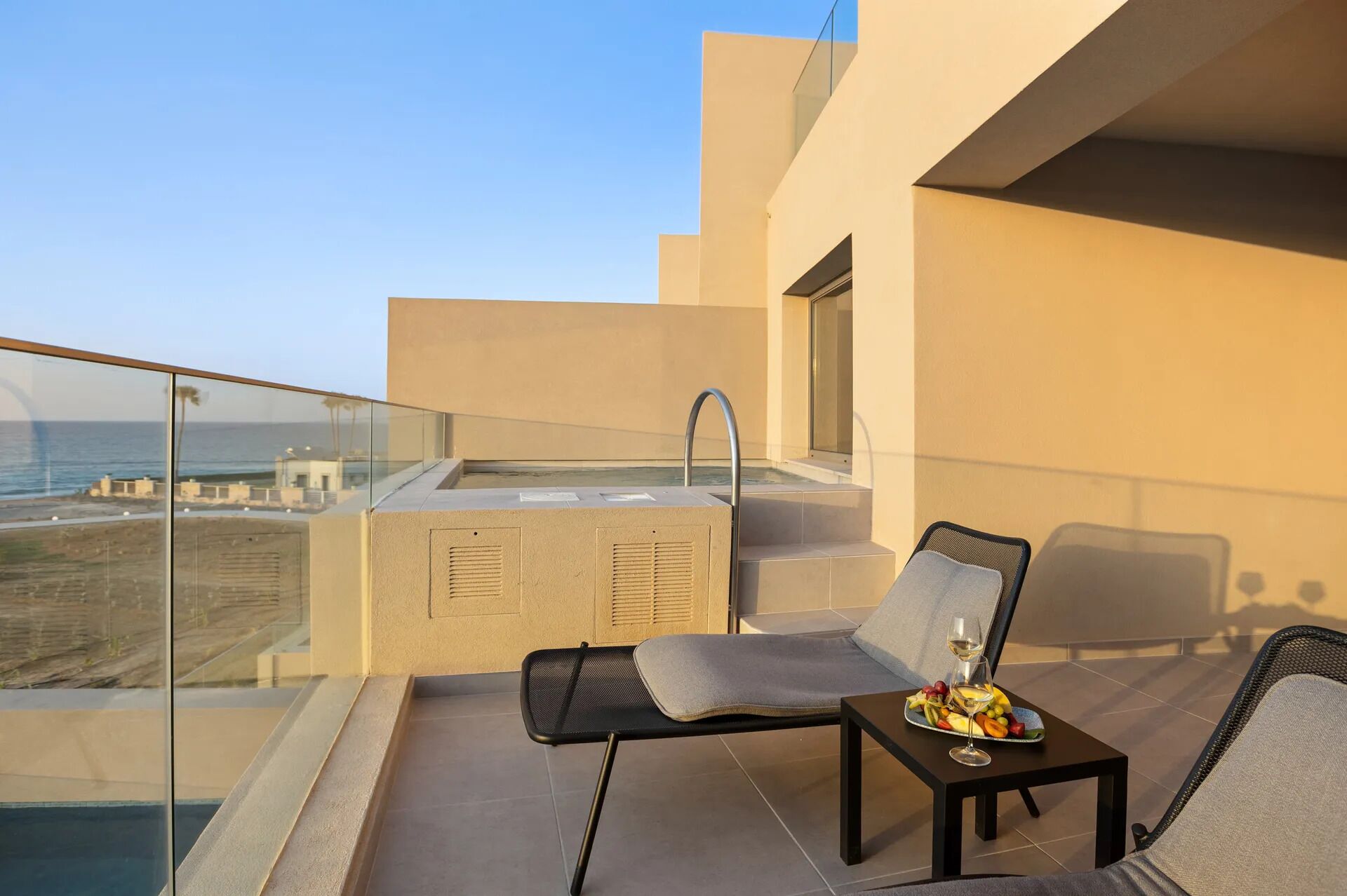 A balcony with a glass railing, a hot tub, and a seating area with a table and chairs.