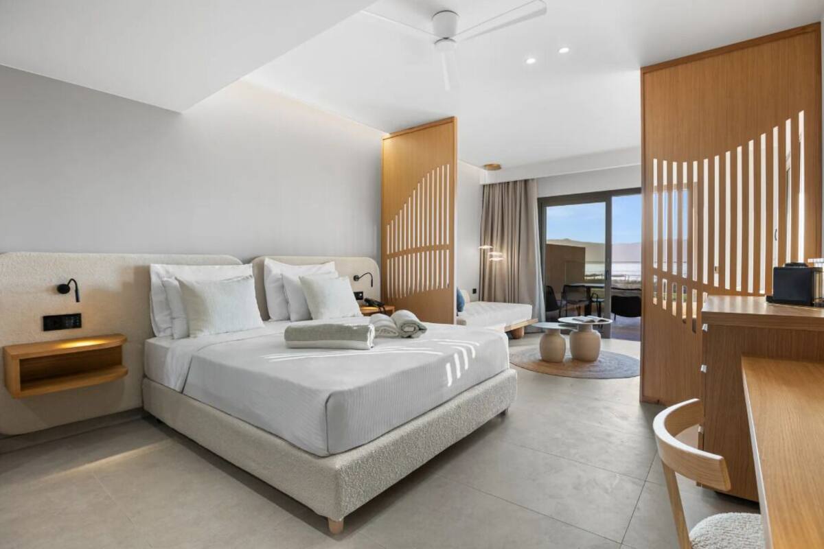 A modern hotel room with a large bed, a desk, and a view of the outdoors.
