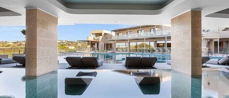 A modern indoor pool with clear water, lounge chairs, and a view of a building with multiple balconies.