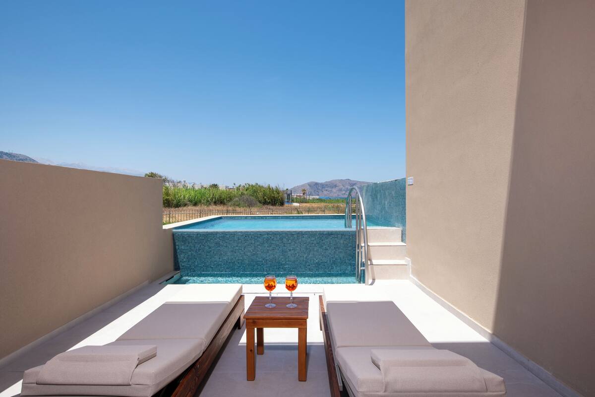 A rooftop pool area with lounge chairs and a table, overlooking a pool with a clear view of the mountains.