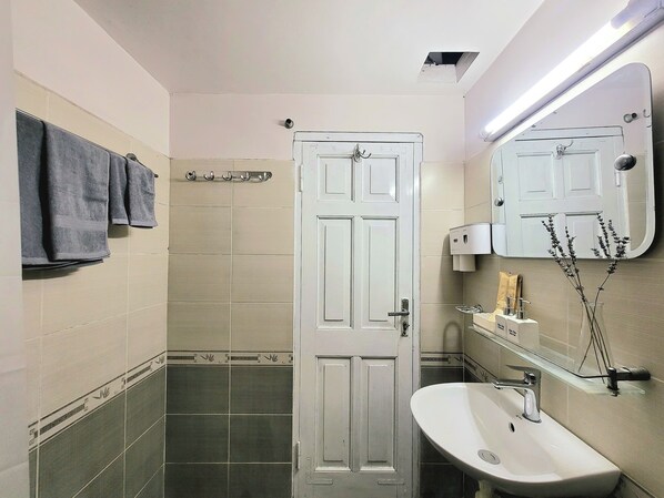 A bathroom with a white door, a sink, a mirror, and towels on a rack. - Tiny homes  (Hanoi)