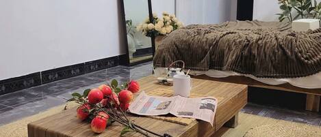 Un dormitorio moderno con una cama, una mesa de centro de madera con manzanas y periódicos, un espejo y un atrapasueños colgante.