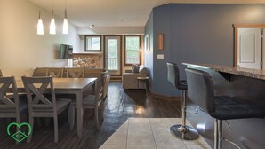 A modern kitchen with a bar area, a dining table with chairs, and a stone accent wall. - 2 BDRM Condo - Superb Facilities - Great Location (Fernie)