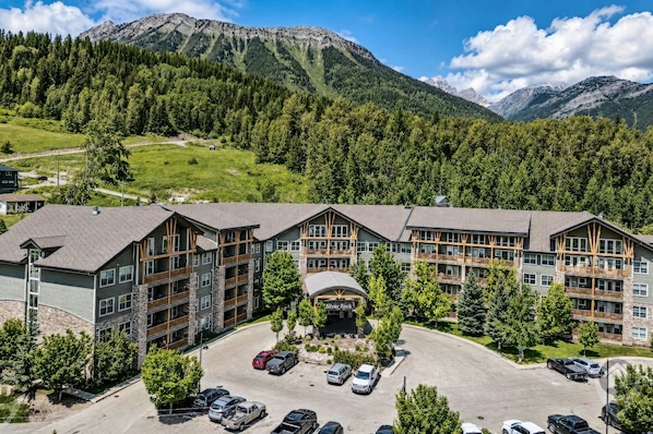 A multi-story hotel with a parking lot, surrounded by forested hills and mountains.