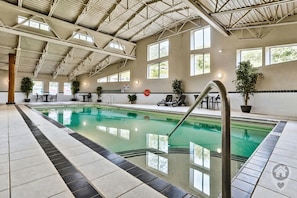 Una piscina interior con agua cristalina, rodeada de suelo de baldosas y plantas en macetas.
