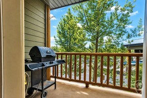 A balcony with a barbecue grill and a view of trees and a parking lot.