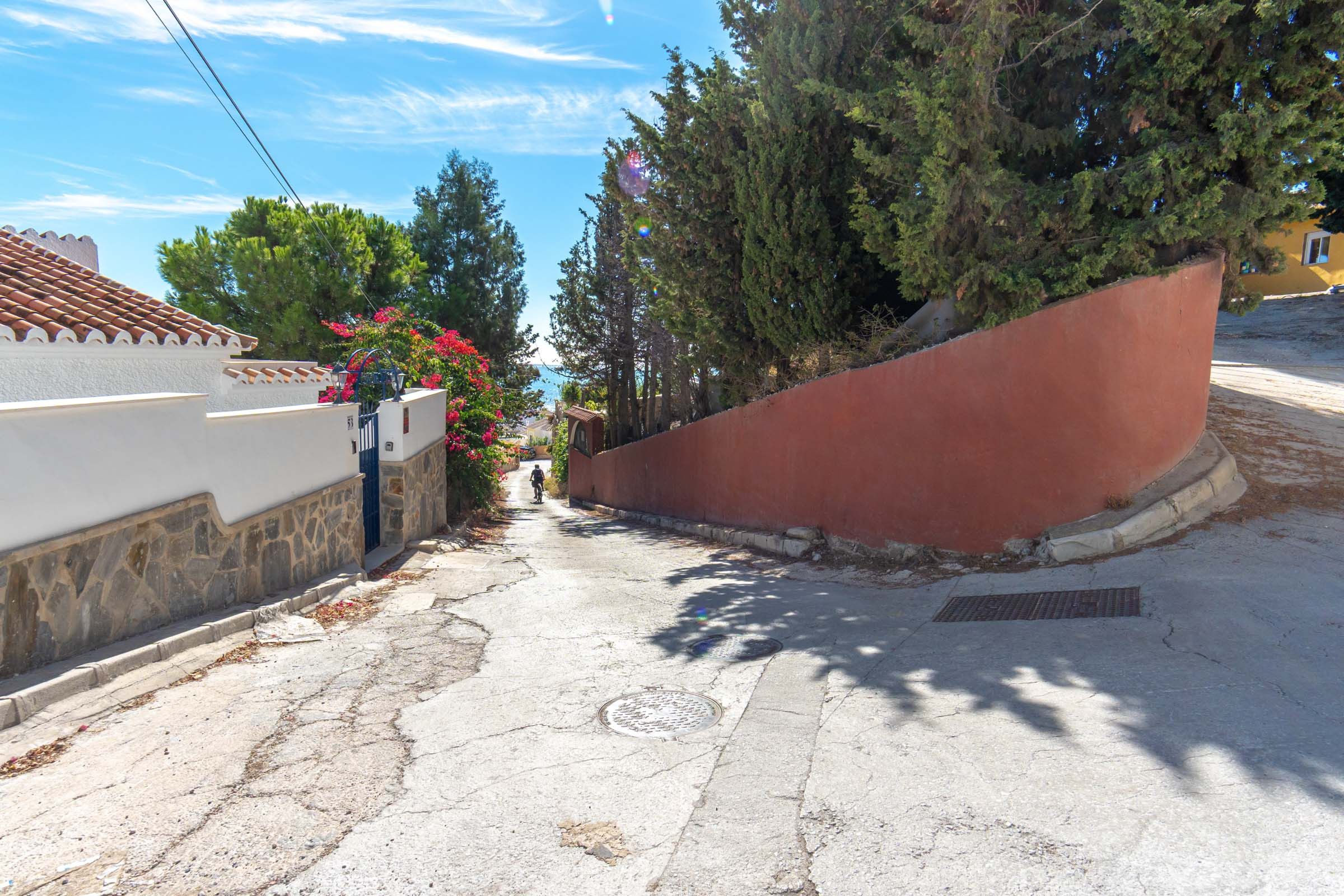 A narrow street with a white building on the left and a red wall on the right.