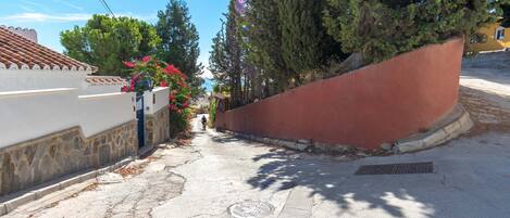 A narrow street with a white building on the left and a red wall on the right.