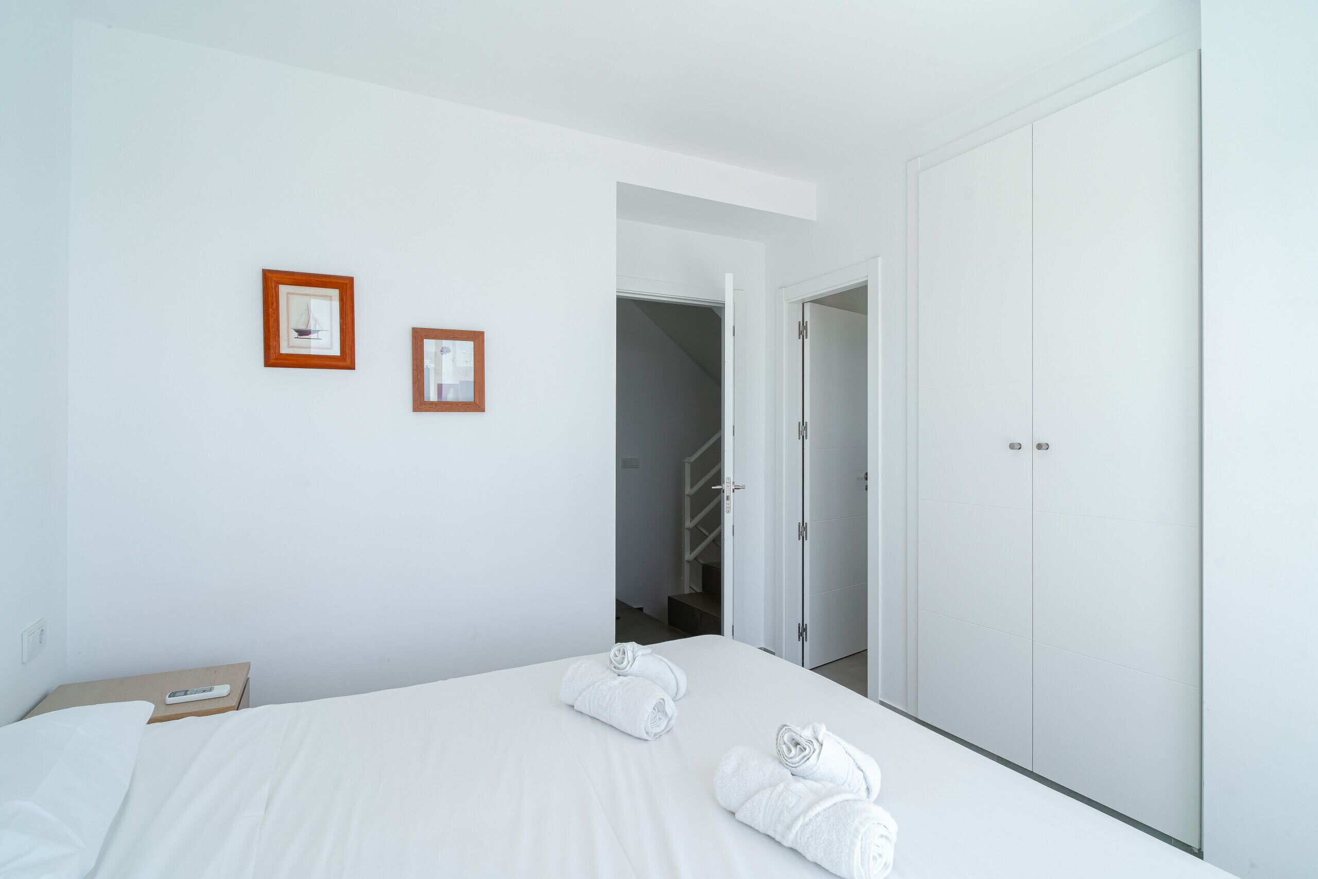 A hotel room with a bed, two framed pictures on the wall, and a wardrobe.