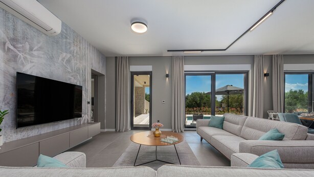 A modern living room with a flat-screen TV, a sofa, a coffee table, and a view of the outdoors. - Villa Intrada ZadarVillas (Sukošan)