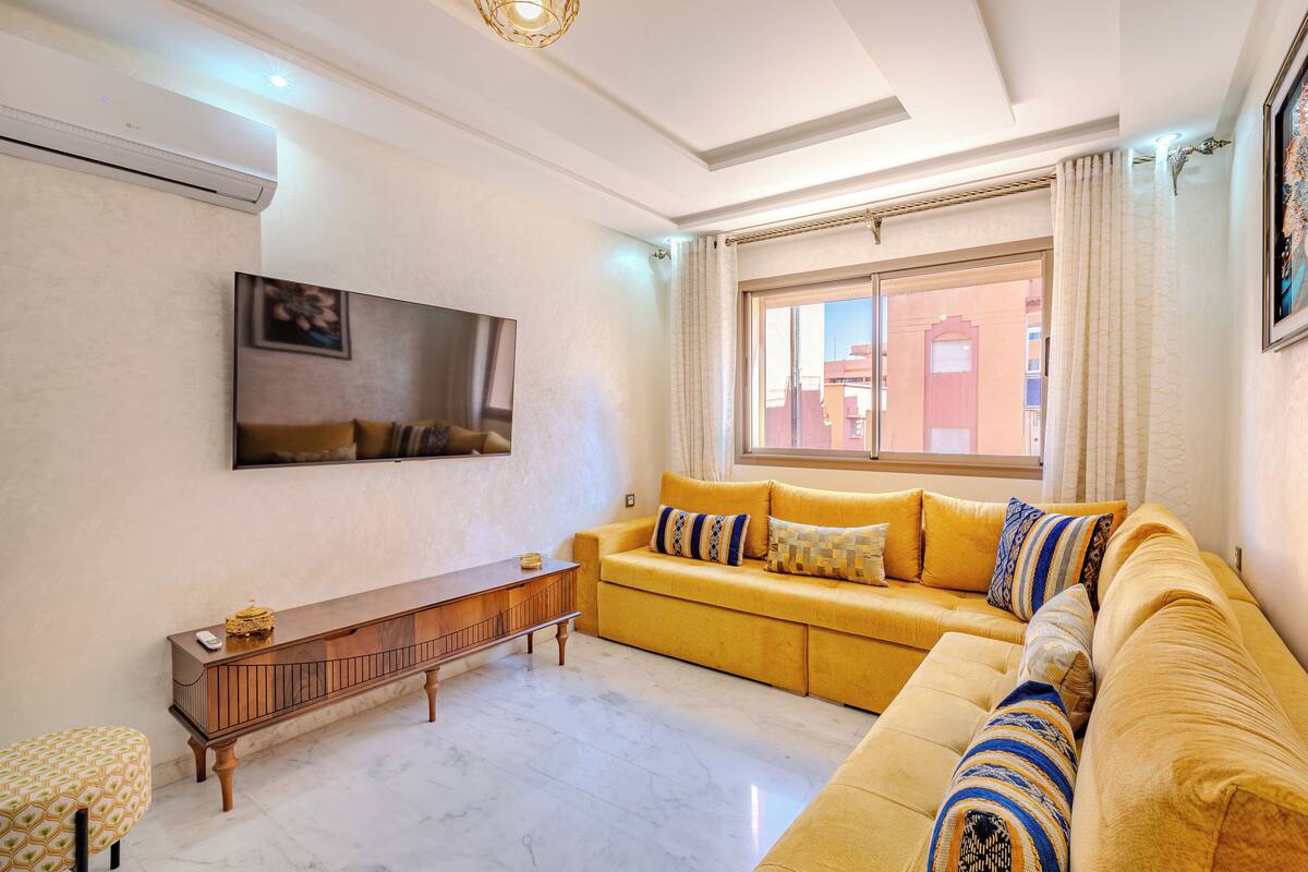 A living room with a yellow sofa, a wooden console table, and a flat-screen TV mounted on the wall.