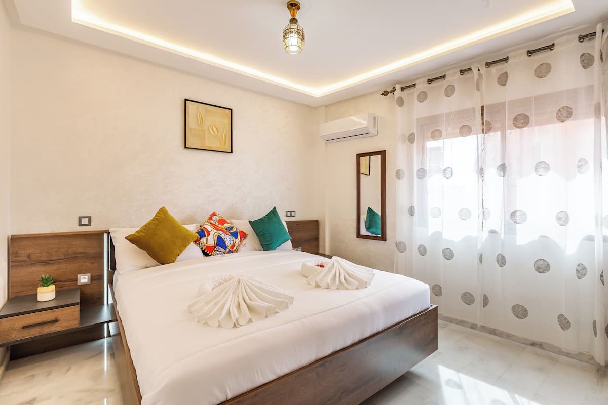 A modern hotel room with a large bed, a nightstand, a small plant, and a ceiling light.