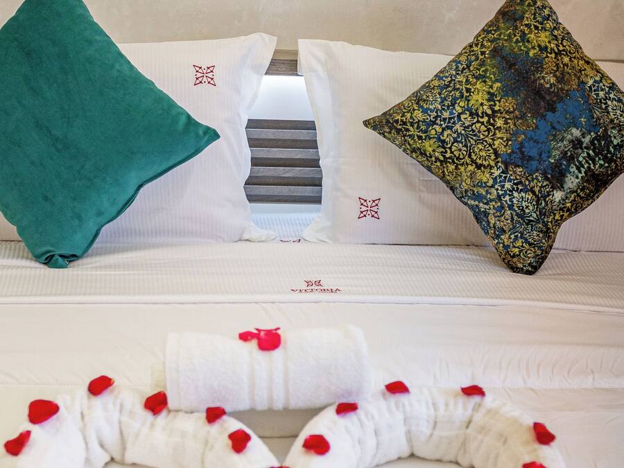 Un lit bien fait, avec une literie blanche, un plaid turquoise et des coussins décoratifs à motifs floraux.