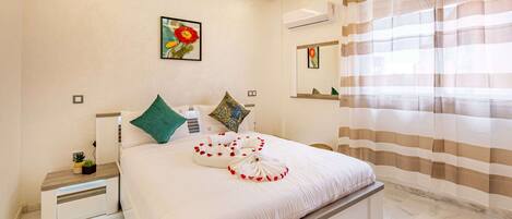 A neatly made bed with a pillow arrangement, a bedside table with a plant, and a painting on the wall.